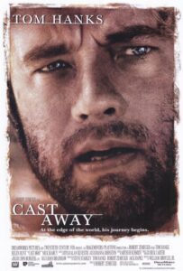 Close-up movie poster of Tom Hanks with a weathered face and intense expression, suggesting survival and isolation. The tagline reads, “At the edge of the world, his journey begins,” and the film title Cast Away is featured in bold white serif font across the lower half.