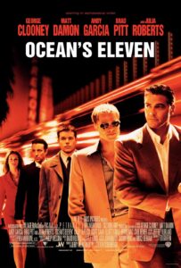 A sleek, orange-hued poster featuring an ensemble cast walking with confident expressions and stylish suits against a backdrop of Las Vegas neon lights. From left to right: Julia Roberts, Andy Garcia, Matt Damon, Brad Pitt (in sunglasses), and George Clooney, who leads the group. The title Ocean’s Eleven appears boldly in white at the center, with actors’ names listed above in a stacked formation.