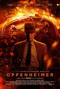 Poster for Oppenheimer directed by Christopher Nolan. Cillian Murphy, in a 1940s-style suit and fedora, stands centered before a fiery backdrop of abstract atomic machinery. The background glows orange and red with sparks and embers, symbolizing nuclear fission and destruction. The text above features the main cast, including Emily Blunt, Matt Damon, Robert Downey Jr., and Florence Pugh. Below, the tagline reads: “Shot with IMAX Film Cameras.”
