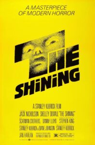 Poster for The Shining featuring a stark yellow background with black block text spelling the title. The word “THE” is stylized with a halftone image of a frightened face emerging from within the letters. Above it reads the tagline: “A masterpiece of modern horror.” The design evokes a sense of dread with minimalist boldness.