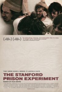 Poster for The Stanford Prison Experiment featuring a chaotic and violent scene where several young men, dressed as prisoners and guards, are engaged in a struggle. One guard appears to punch a prisoner against a wall while others crowd around. The tagline at the bottom reads: “They were given 2 weeks. It lasted 6 days.” The film title is printed boldly in red on a crumpled paper-textured background, and the subtitle notes it is “based on true events.” A quote above the title praises the film’s disturbing realism.