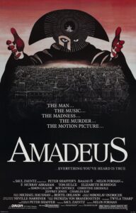 Poster for Amadeus featuring a dark, masked figure with outstretched hands looming over an illuminated cityscape. The figure’s eyes peer through an ornate circular headdress, creating an ominous, theatrical image. Beneath the city appears the title Amadeus in large white letters, with the tagline “Everything you’ve heard is true.” The dramatic black-and-red design reflects the film’s themes of musical genius, obsession, rivalry, and psychological conflict.